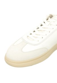 White sneaker featuring a mix of smooth leather and suede, round toe, and a rubber sole with a textured pattern. Laces and padded tongue included.