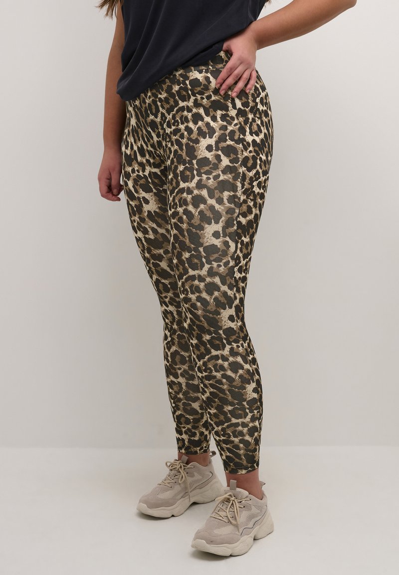 Leggings en imprimé léopard dans des nuances d'or et de noir, présentant un design ajusté et une texture lisse, associés à des baskets gris clair.