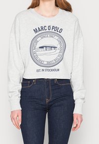 Grijze cropped sweatshirt met een ronde halslijn, voorzien van een grafische print in marineblauw. Gecombineerd met donkerblauwe denim jeans en zichtbare manchetten.