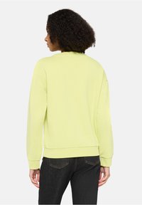 Jasnożółta bluza z długimi rękawami i okrągłym dekoltem, charakteryzująca się luźnym krojem i ściągaczami przy mankietach, zestawiona z ciemnymi dżinsami.