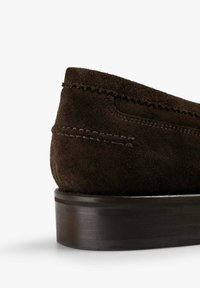 Zapato cómodo de ante marrón sin cordones, con un diseño redondeado, suela de cuero oscura en contraste y detalle de costura visible a lo largo del borde superior.