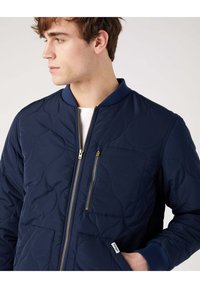 Granatowa pikowana kurtka bomberka z zamkiem błyskawicznym, prążkowanym kołnierzem i mankietami, oraz małą przednią kieszenią z ozdobnym złotym zamkiem.