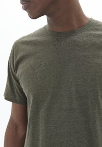 Tricou scurt cu mânecă, de culoare verde măsliniu, fabricat dintr-un material moale și texturat. Conține un guler rotund și dungi orizontale subtile.
