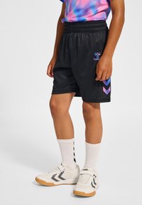 Svarta träningsshorts med elastisk midja, prydda med blå och rosa zigzag-accenter, tillsammans med vita skor och svarta och vita strumpor.