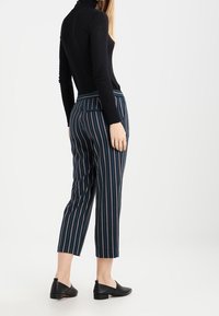 Randiga byxor i marinblått med röda och vita accenter, med en smal passform och ankellång design, kombinerat med en svart långärmad topp.