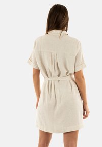 Abito in lino beige corto con maniche corte, colletto e vita con cintura. Presenta un dettaglio plissettato sul retro per un tocco di consistenza aggiuntivo.