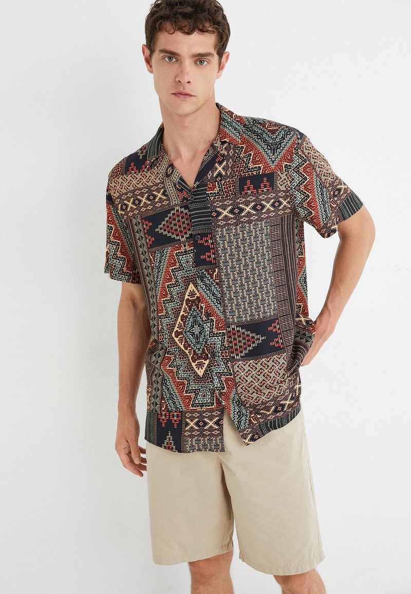 Camisa de manga corta con un diseño de múltiples patrones en rojo, azul y negro, que presenta formas geométricas y un ajuste relajado.