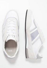 Vita och gråa träningssneakers med en design av mocka och mesh, rundade tår, snörning och en svart gummisula. Har logotyp på tungan.