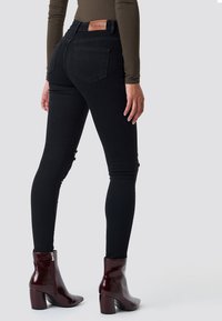 Czarne jeansy skinny z wysokim stanem, z tylnymi kieszeniami, lekko przetarte na kolanach, w połączeniu z błyszczącymi burgundowymi botkami za kostkę.