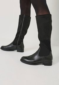 Black knee-high boots with a glossy leather lower section, matte suede upper, and side zipper detailing. Flat sole and rounded toe design.