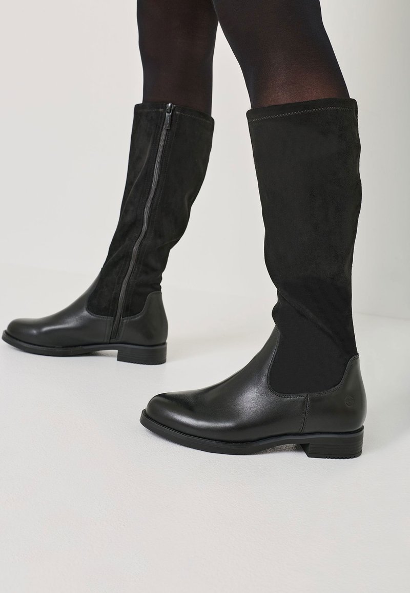 Black knee-high boots with a glossy leather lower section, matte suede upper, and side zipper detailing. Flat sole and rounded toe design.