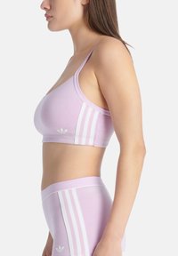 Svetle fialová sportovní podprsenka s tenkými ramínky, která má po boku bílé trojpruhy a malé logo ve spodní části.