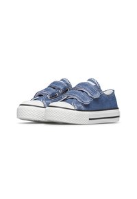 Scarpe slip-on in denim blu con suole in gomma bianche, dotate di due cinghie regolabili e dettagli di cucitura bianchi.