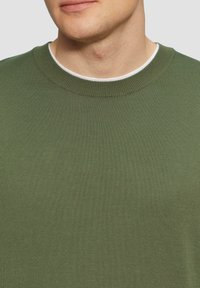 Oliwkowy sweter dzianinowy z ribbanym okrągłym dekoltem. Posiada gładką fakturę, dopasowany krój oraz minimalne detale w szwach.