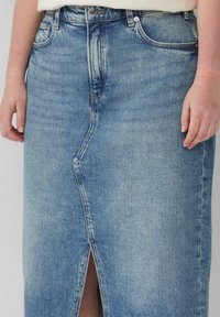 Jupe en denim bleu clair avec une fente sur le devant, dotée de poches et d'un design classique à cinq poches. Le tissu présente une finition légèrement texturée.