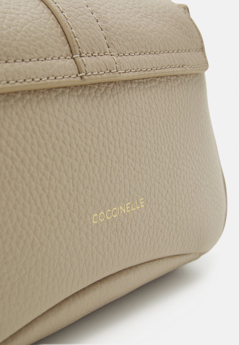Beige Lederhandtasche mit strukturierter Oberfläche, ausgestattet mit goldenen Logo-Akzenten und einem schlichten, geschwungenen Design.