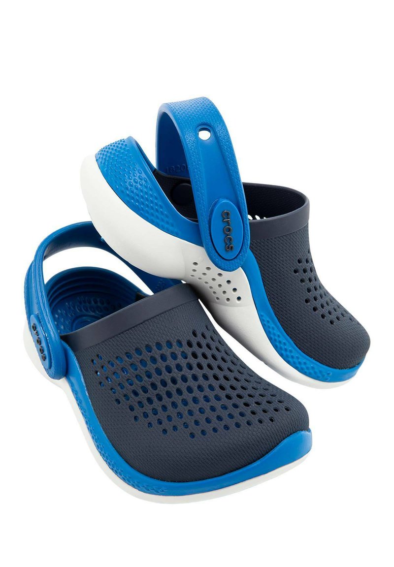 Zuecos azules y marinos con un diseño perforado, suela blanca y una correa en el talón ajustable, fabricados con material ligero e impermeable.