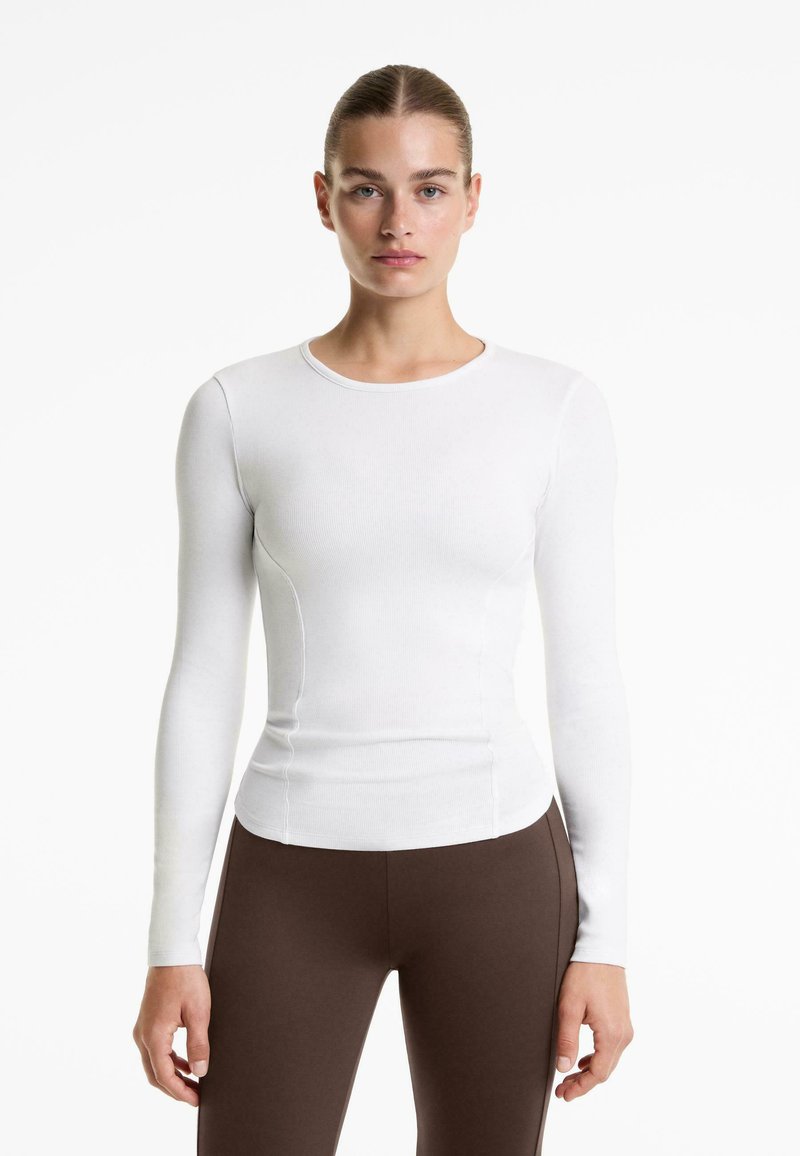 Cămașă albă cu mânecă lungă, ajustată, cu guler rotund, textură cu striații și detalii de cusătură, asortată cu leggings maro.