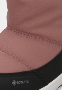 Vandeniui atspari rožinė batai su tekstūruota audinio viršutine dalimi, sustiprinta juoda gumine padanga ir matoma Gore-Tex prekės ženklo žymė. Yra siuvinėjimo detalės.