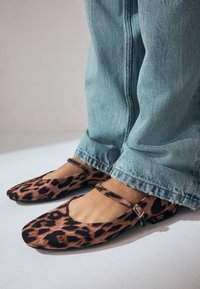 Ballerines à imprimé léopard avec un bout rond et une sangle à la cheville, en tissu doux, associées à un jean évasé bleu clair.