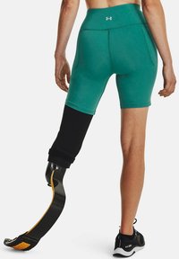 Pantalones cortos deportivos verdes con un diseño ajustado. Presentan una cintura alta y una pierna protésica negra con detalles amarillos.