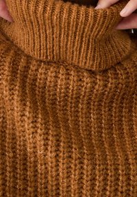 Mains ajustant le col roulé côtelé et épais en tricot marron d'un pull duveteux.