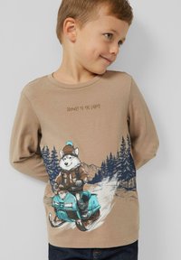 Junger Junge trägt ein beiges Langarmshirt mit einem Grafikdruck eines Hundes in einem Hut, der auf einem blauen Schneemobil durch verschneite Kiefern fährt.