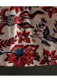 Tela floral con patrones en rojo, azul y negro sobre un fondo crema. Presenta costuras delicadas y una pequeña etiqueta metálica.