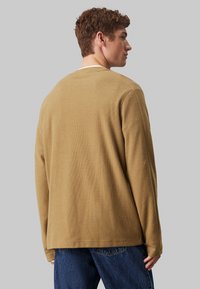 Jersey marrón de manga larga con tejido texturizado, corte holgado, escote redondo y costuras en contraste, combinado con jeans de mezclilla azul.