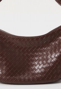 Καφέ υφαντή δερμάτινη τσάντα χειρός με λεία επιφάνεια, στρογγυλεμένο σχήμα και φερμουάρ κατά μήκος της πάνω ακμής. Διαθέτει υφασμένη επιφάνεια.