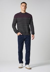 Pull en tricot rayé gris et violet foncé avec un col rond, associé à un jean bleu foncé et des baskets blanches. Le modèle se tient les mains dans les poches.