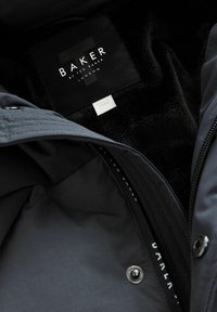 Gros plan sur une veste noire Ted Baker London montrant l'étiquette intérieure et la doublure noire douce avec une coque extérieure grise et des détails de boutons-pression.