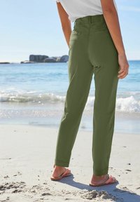 Oliwkowe, proste spodnie z wysokim stanem, tylnymi kieszeniami i mankietami, w połączeniu z klapkami na piaszczystej plaży blisko wody.