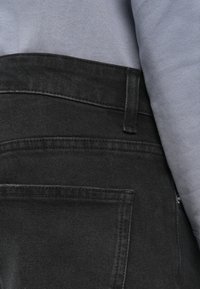 Μαύρο τζιν από τζην ύφασμα με υφή, διαθέτει πίσω τσέπη και γκρι μπλούζα που διακρίνεται μερικώς πάνω από τη μέση της ζώνης.