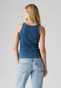 Débardeur bleu côtelé avec une coupe ajustée, présentant de larges bretelles et une texture lisse, associé à un jean en denim bleu clair.