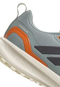 Zapatilla deportiva gris con material repelente al agua, detalles texturizados en naranja y gris, y una suela blanca de goma con un dibujo de tracción.