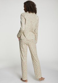 Frau steht barfuß in cremefarbenem Schlafanzug, bedeckt mit kleinen roten und weißen Zuckerstangenmustern, mit dem Rücken zur Kamera.