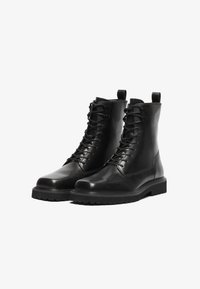 Botas de tobillo de piel negra con un acabado suave, que presentan un diseño de cordones, punta redonda y suela de goma resistente con tracción.
