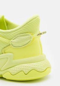 Neonin keltainen lenkkikenkä, jossa on teksturoitu päällinen, pyöreä kantapää, pehmustettu kaulus ja kumipohja kuvioidulla urituksella.