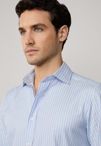 Camisa abotonada de rayas azul claro con cuello, diseño ajustado y textura de algodón suave con acentos blancos y un sutil brillo.