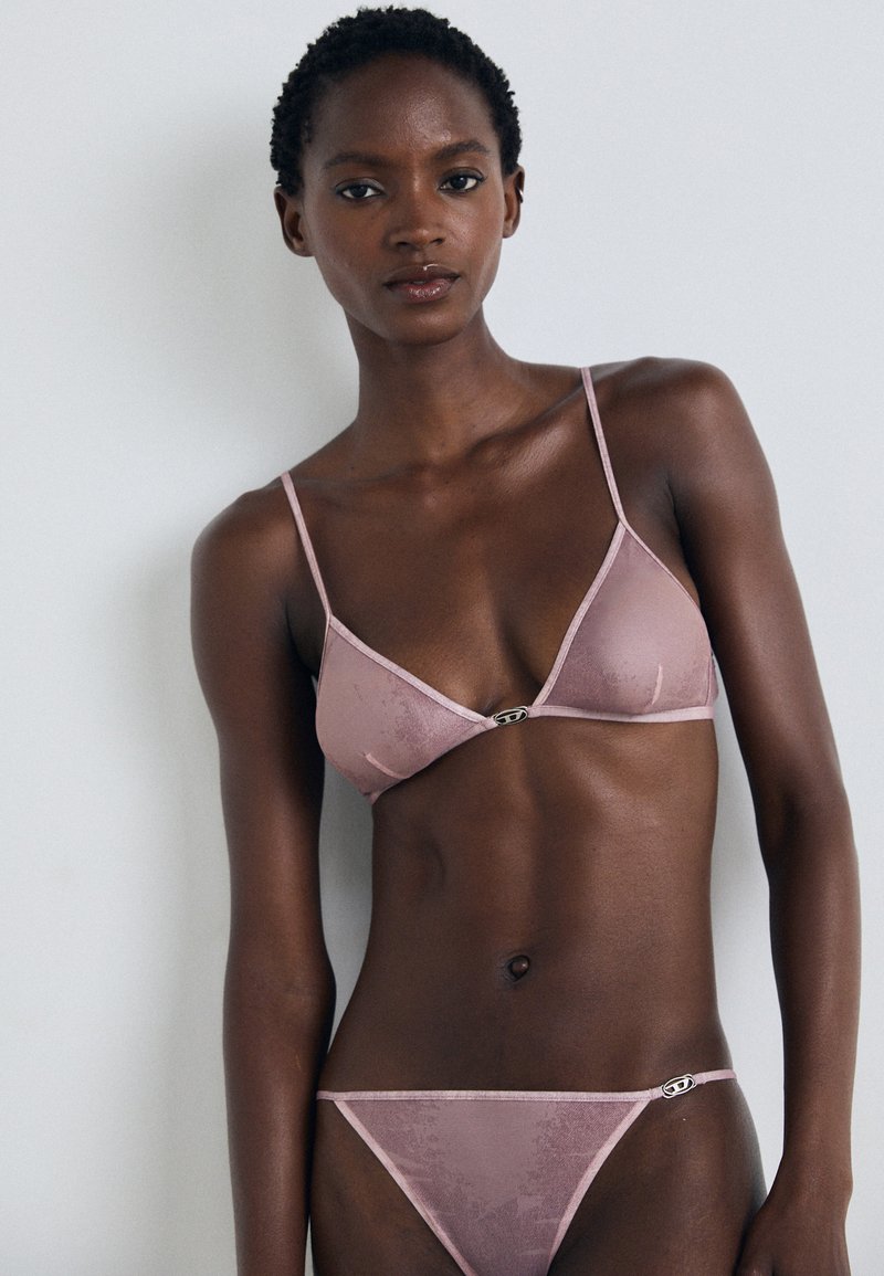 Lichtroze fluwelen bikini set met een driehoekige bralette met verstelbare bandjes en een klein hardware accent in het midden. Getextureerde afwerking.