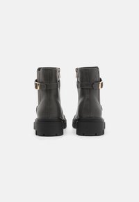 Bottes en cuir gris foncé jusqu'aux chevilles avec une semelle noire épaisse, des fermetures éclair sur les côtés et des sangles à boucle dorée pour un détail supplémentaire.