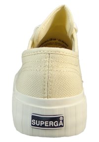 Kremowe płócienne buty wsuwane o teksturowanej powierzchni, biała gumowa podeszwa oraz niebieska metka marki na pięcie. Prosty i funkcjonalny design.