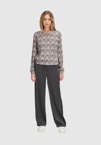 Blusa a maniche lunghe beige con stampa geometrica, abbinata a pantaloni larghi grigi scuri e sneakers bianche. Tessuto morbido e vestibilità rilassata.