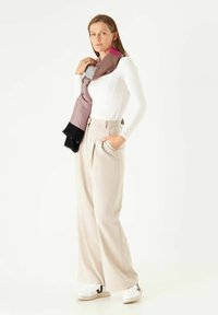 Lichte, multicolore sjaal hangt over een figuur in een strak wit topje en ruime, beige broek, gecombineerd met witte sneakers.