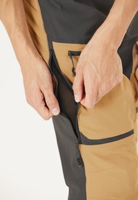 Waterdichte broek met een twee-kleurig ontwerp in zwart en lichtbruin. Voorzien van een ritszak met gaasvoering. Lichtgewicht stof.