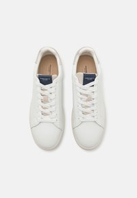 Vita lädersneakers med en slät yta, beige detaljer och en marinblå tungslabel. Har platta snören och en rundad tådesign.