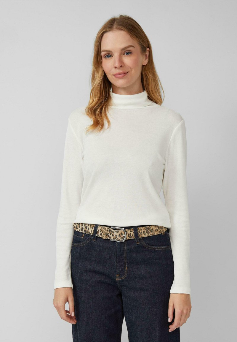 Witte langmouw turtleneck trui gecombineerd met donkere spijkerbroek en een leopardenprint riem, met een gladde textuur en een getailleerd ontwerp.
