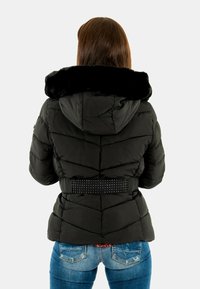 Chaqueta acolchada negra con cuello de piel sintética, cintura con cinturón adornado con piedras brillantes y patrón acolchado en forma de chevrón. Se ven jeans de mezclilla debajo.