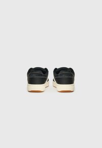 Black sneakers with a leather upper, cream rubber sole, and a gum outsole. Features a textured pattern on the heel and "CONVERS" branding.